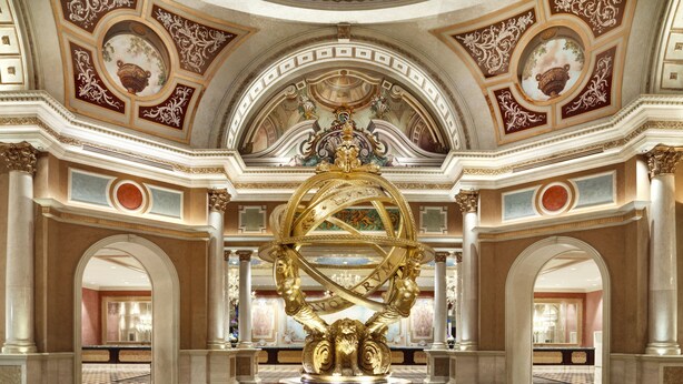 A grand lobby with a central fountain, ornate ceiling, and marble flooring.