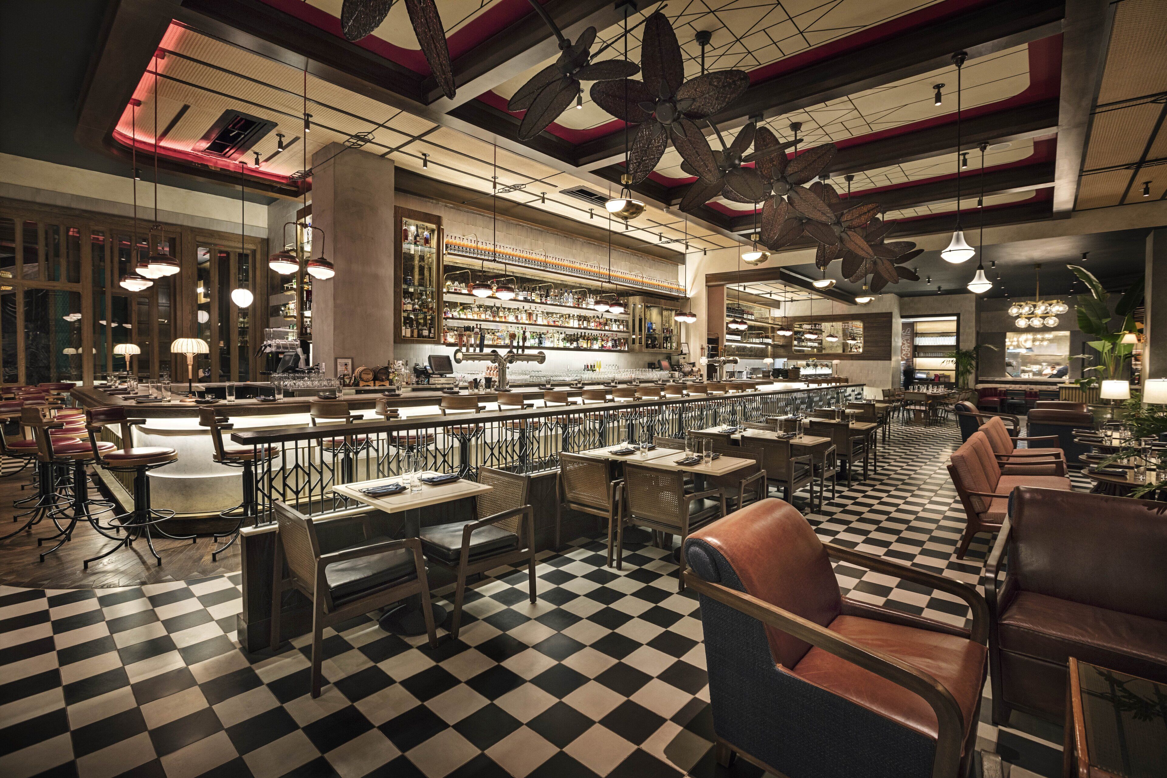A spacious restaurant with a checkered floor, multiple dining areas, and a bar.