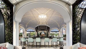 A bar area with a high ceiling and arches, featuring a central bar counter with stools and a seating area with sofas.