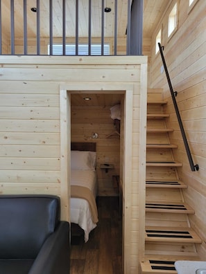 Cozy cabin-style accommodation with a single bed, wooden staircase, and a comfortable sofa.