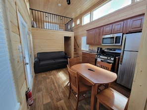 Cozy living space with a loft area, featuring a sofa, dining table, and kitchenette.