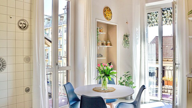 Un coin repas avec une table ronde, des chaises, un vase de fleurs et une vue sur l’extérieur.