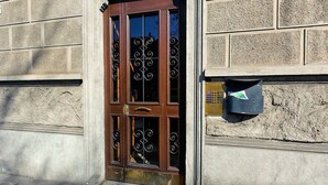 Une porte en bois avec un panneau de verre et des éléments décoratifs en fer forgé, une boîte aux lettres et un mur en pierre à la texture particulière.