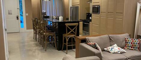 A modern living room with a sofa set, a dining area with chairs, and a kitchen with wooden cabinets.