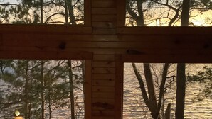 En stuga av trä med ett stort fönster, en träveranda och utsikt över ett skogsområde.