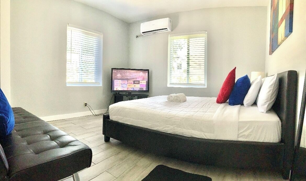 A bedroom with a bed, a television, and a window with blinds.