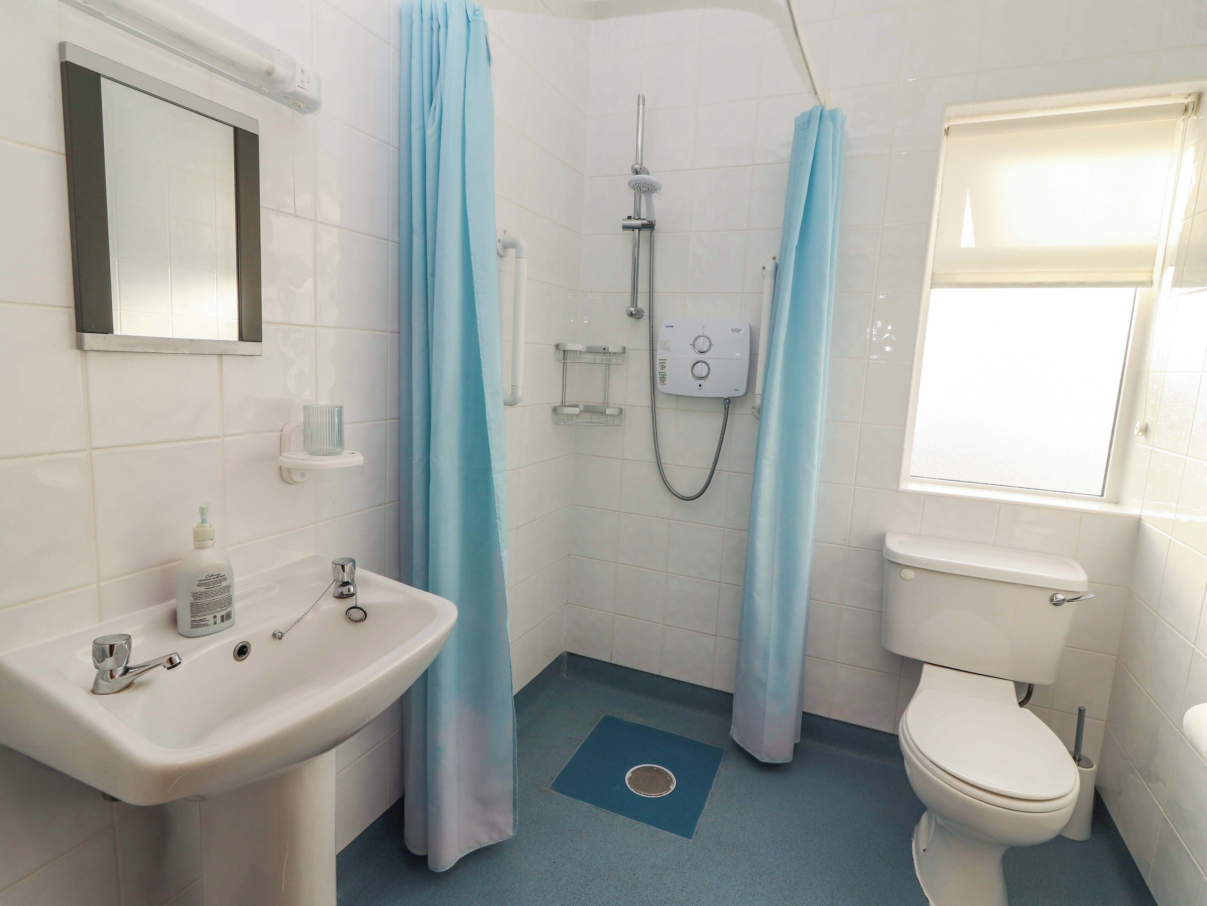 A bathroom with a sink, toilet, shower, and a window.