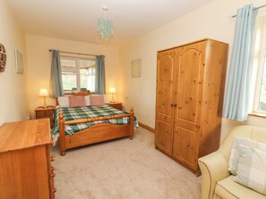 A bedroom with a wooden bed, bedside tables, a wardrobe, a chair, and a window with curtains. - Moybella Lodge (Lisselton)