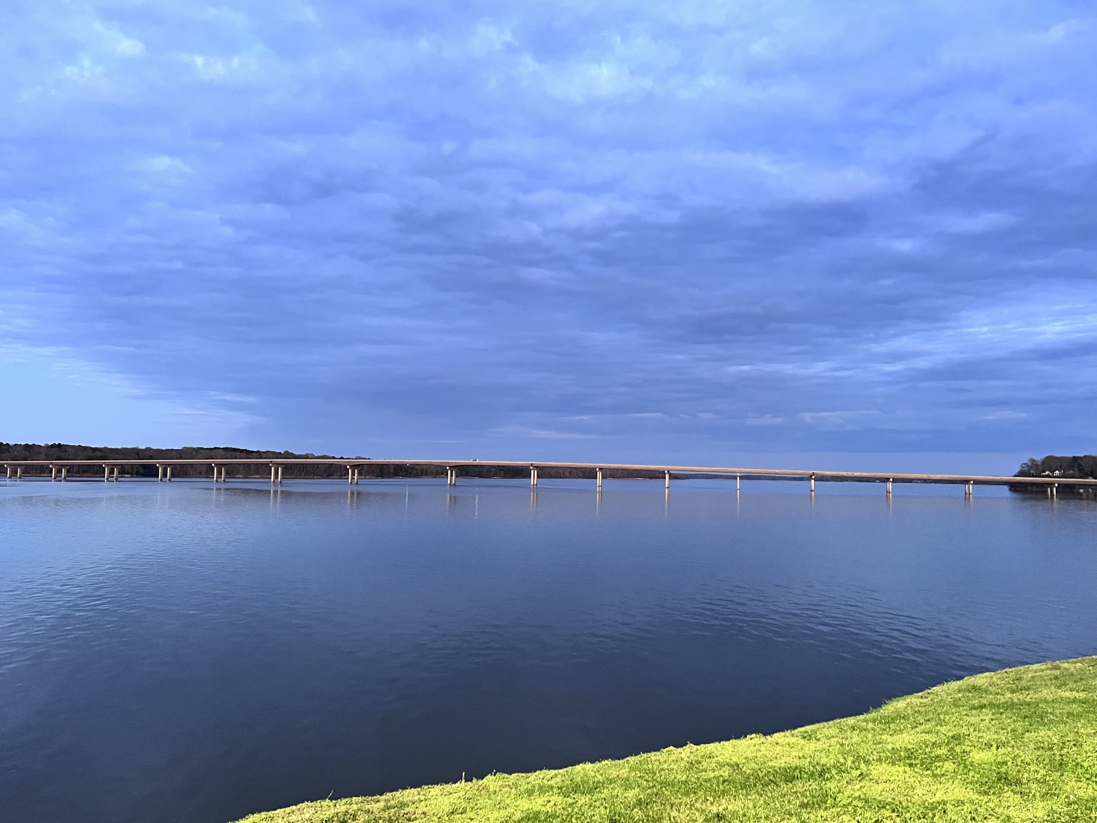 Un lago tranquilo con un puente a lo lejos y un área verde en primer plano.