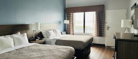 A hotel room with two beds, a ceiling fan, a large window with curtains, and a wooden floor.