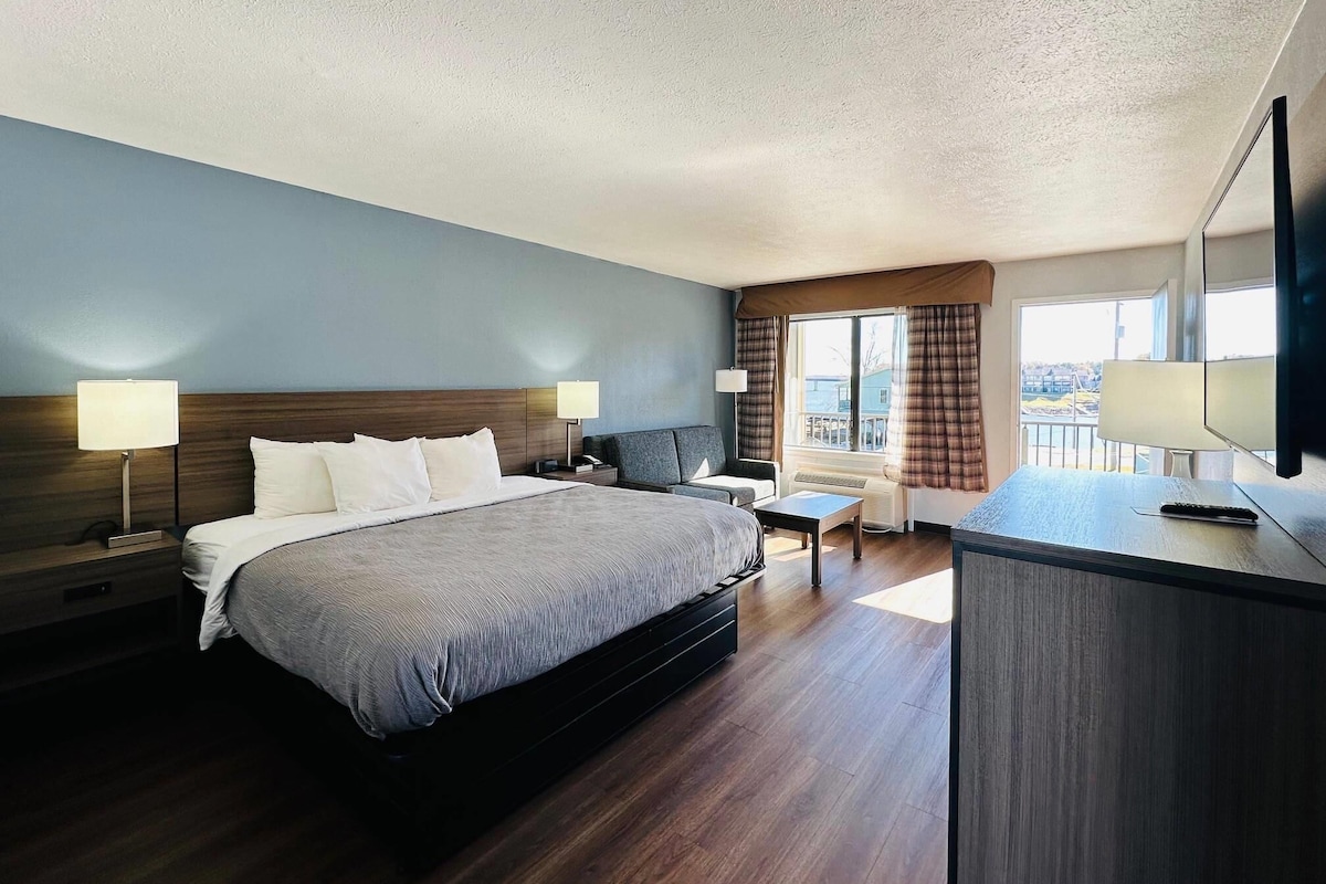 A hotel room with a large bed, a desk, a chair, a TV, and a window with curtains.