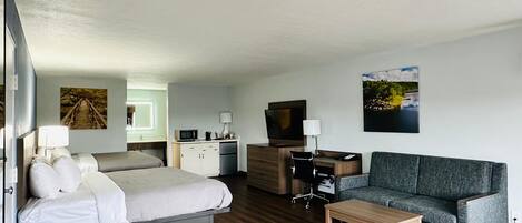 A hotel room with a bed, a sofa, a TV, a desk, and a small table.