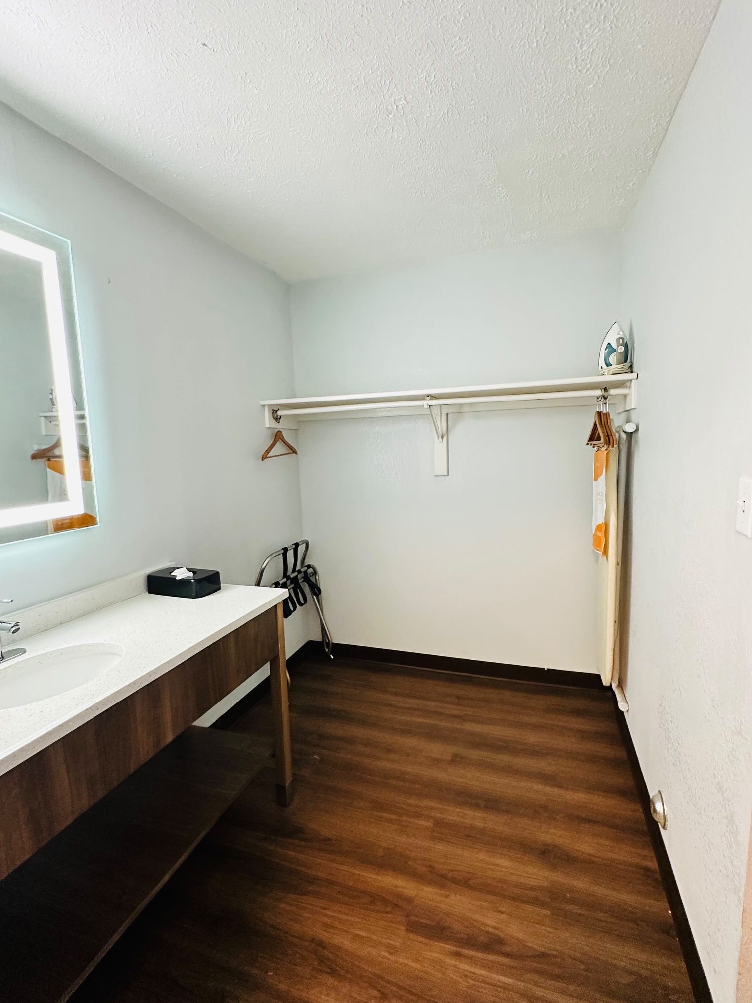 A bathroom with a wooden floor, a white sink, a mirror, and a towel rack.