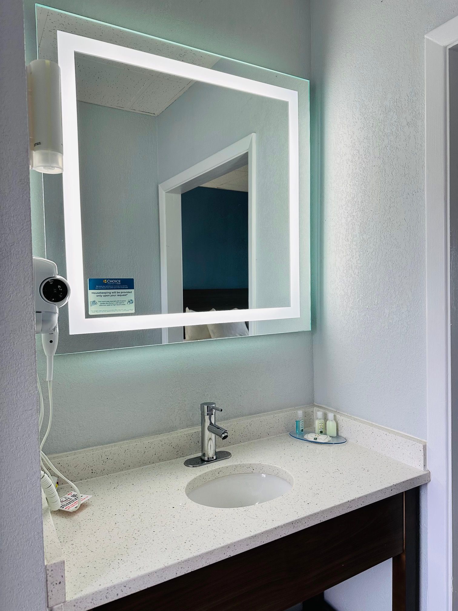A bathroom with a white sink, a mirror with a light, and a security camera.