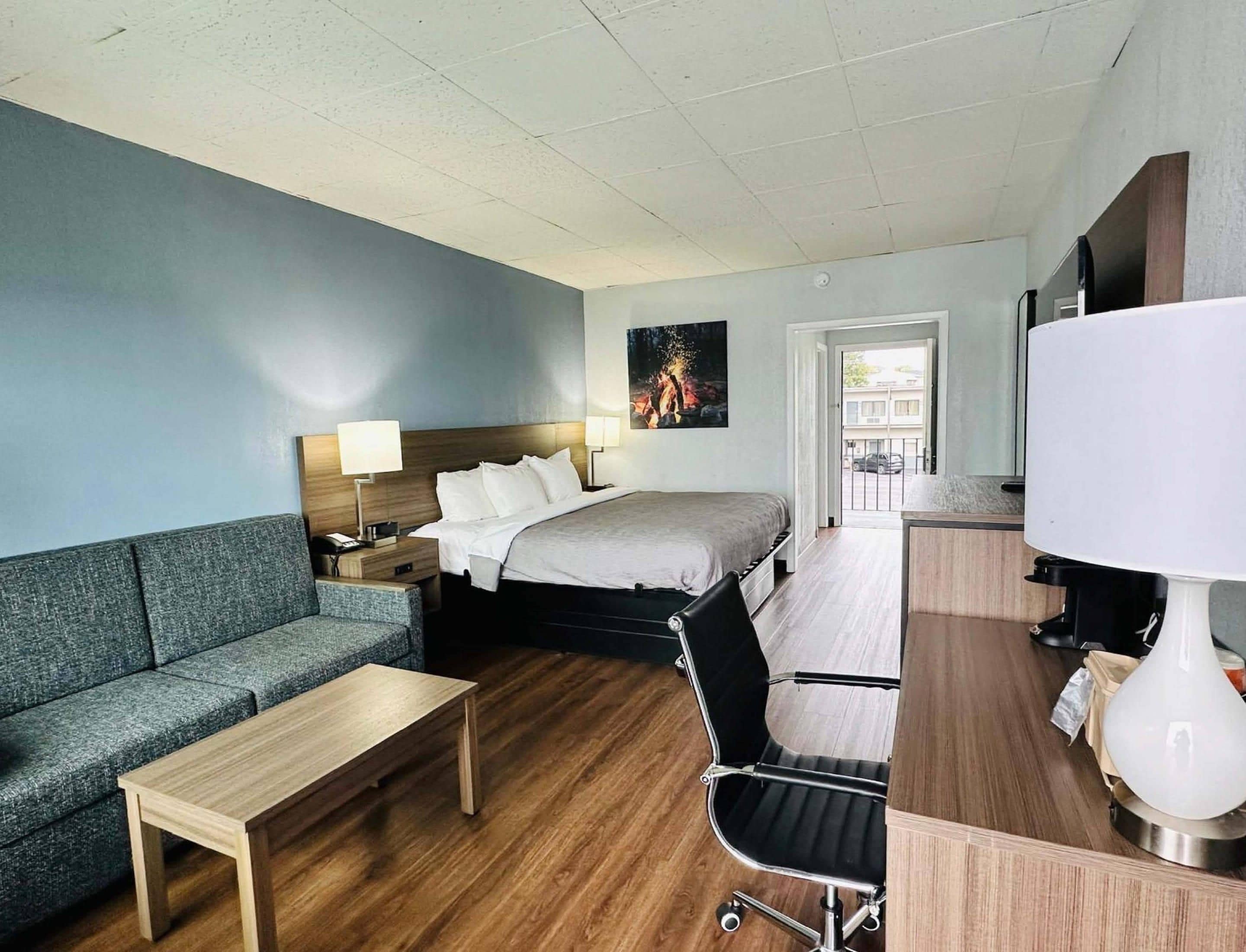 A hotel room with a bed, a sofa, a desk, a chair, and a TV.