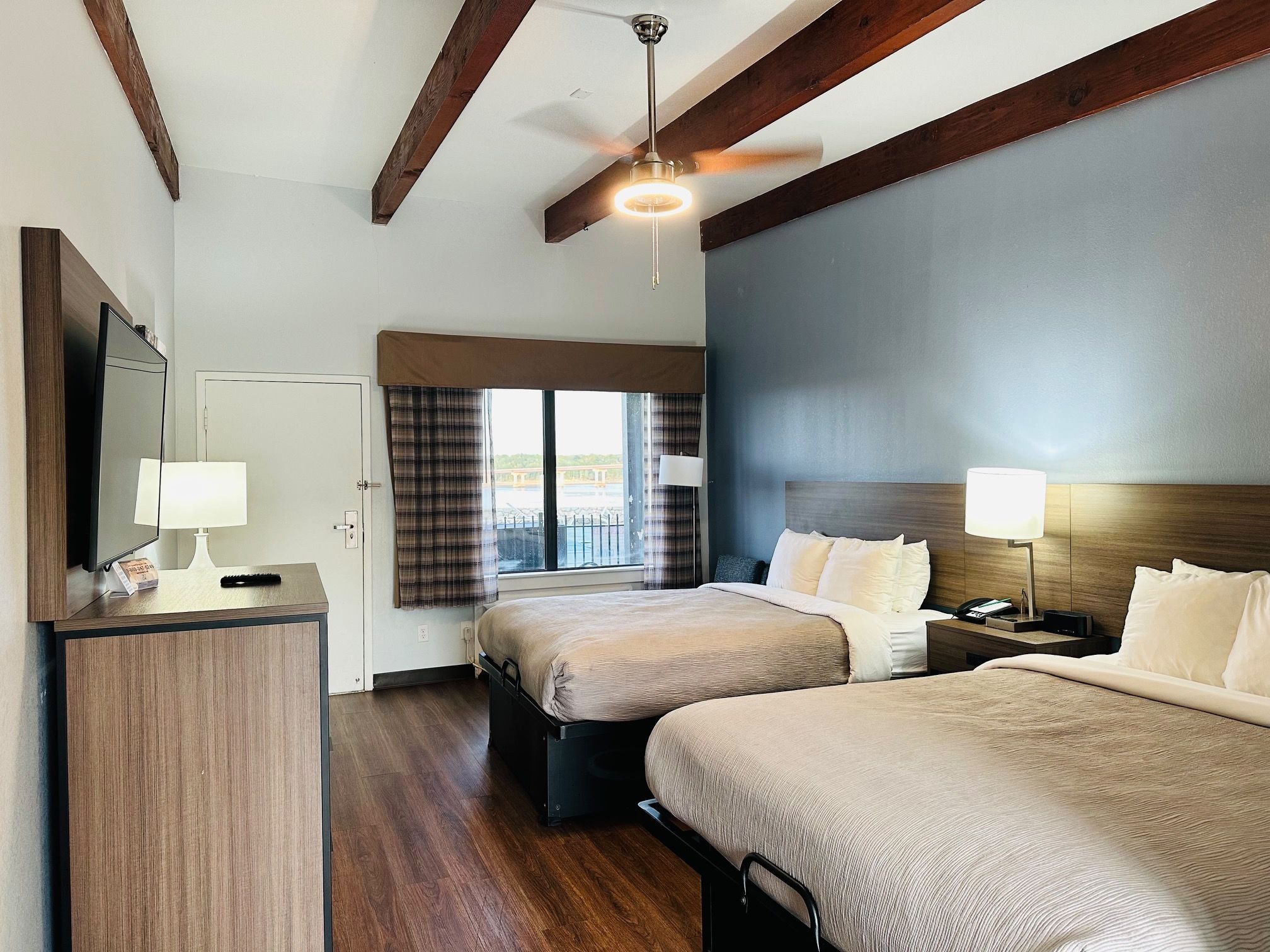 Une chambre d’hôtel avec deux lits, un bureau, un miroir et un ventilateur de plafond.