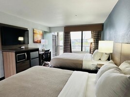 Habitación de hotel con dos camas, un escritorio, una silla, un televisor y una ventana con cortinas.