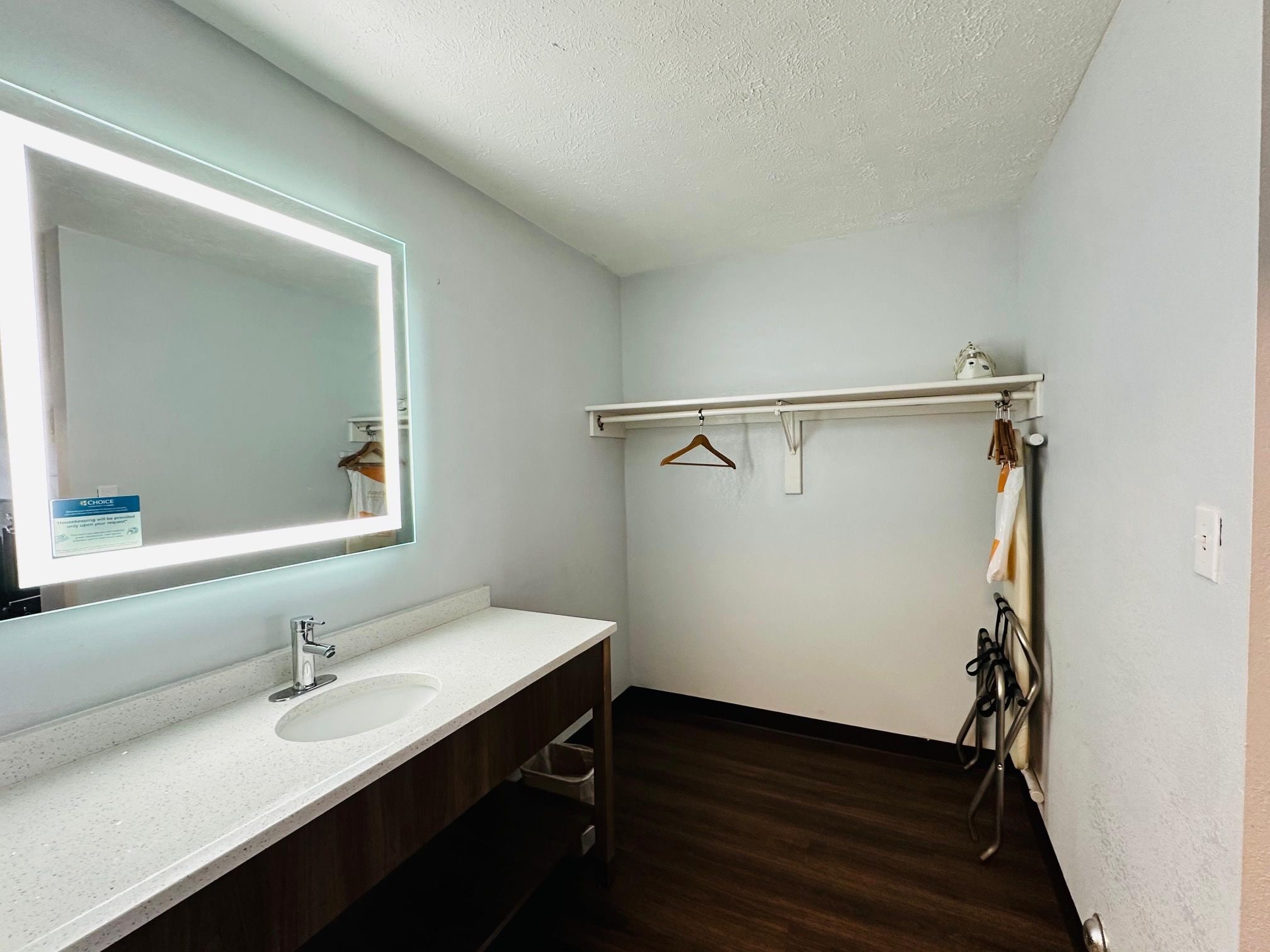 A bathroom with a white sink, a mirror with a light, a wooden vanity, a towel rack, and a shower area.