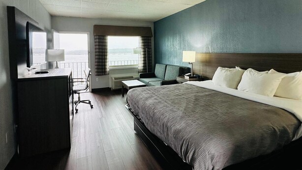 A hotel room with a large bed, a desk with a chair, a TV, and a view of the water.