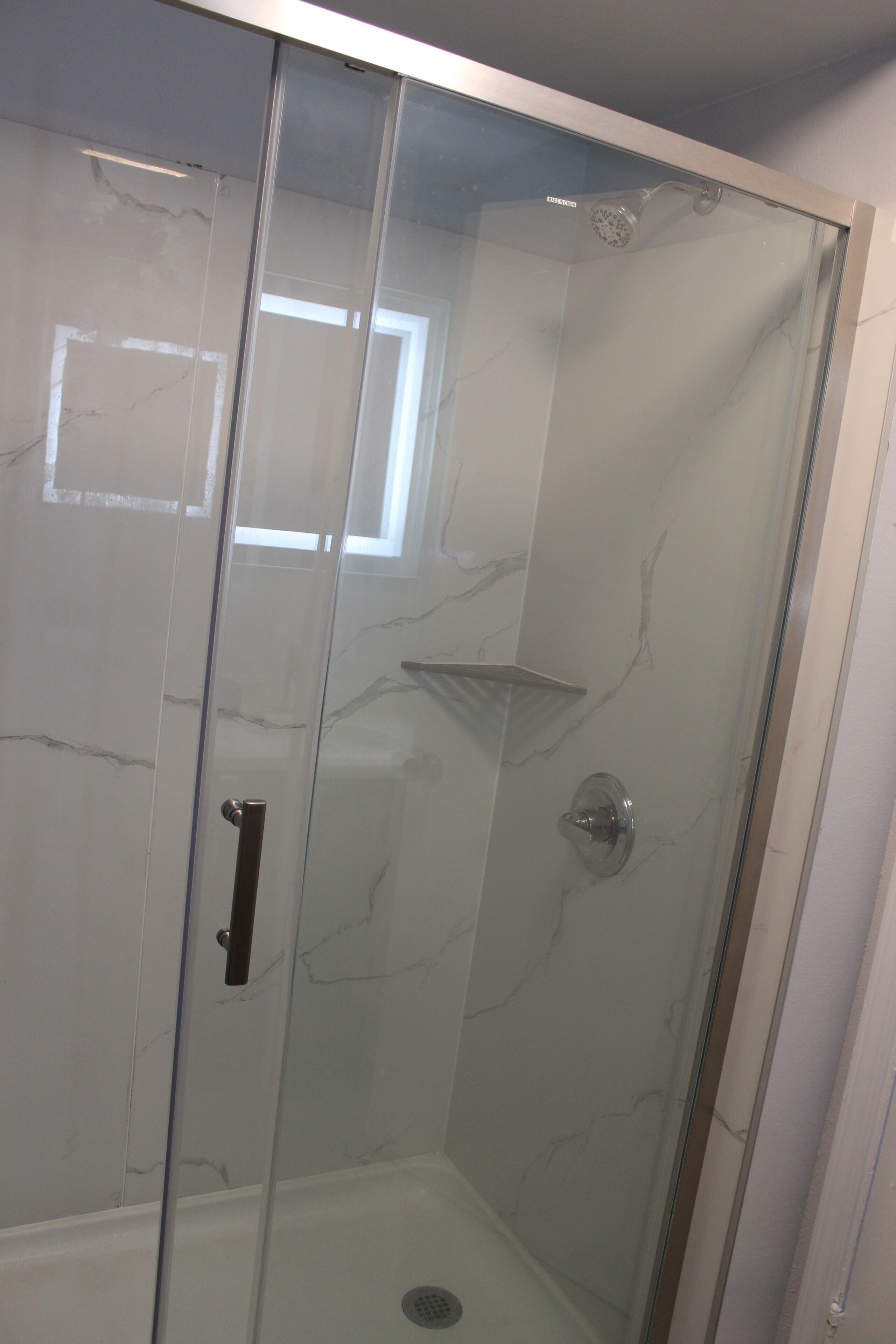 A glass-enclosed shower with a marble wall and a small shelf.