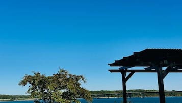 Ein Sitzbereich im Freien am Wasser mit einer Pergola, einem Tisch und einem Grill.