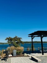 Un área de estar al aire libre frente al agua, con una pérgola, una mesa y una parrilla.