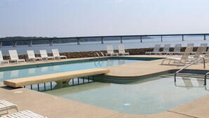 A pool with lounge chairs and a stone wall, overlooking a bridge and water.