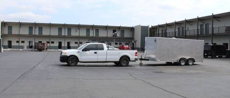 A white pickup truck towing a trailer in an industrial parking lot with a large building in the background.