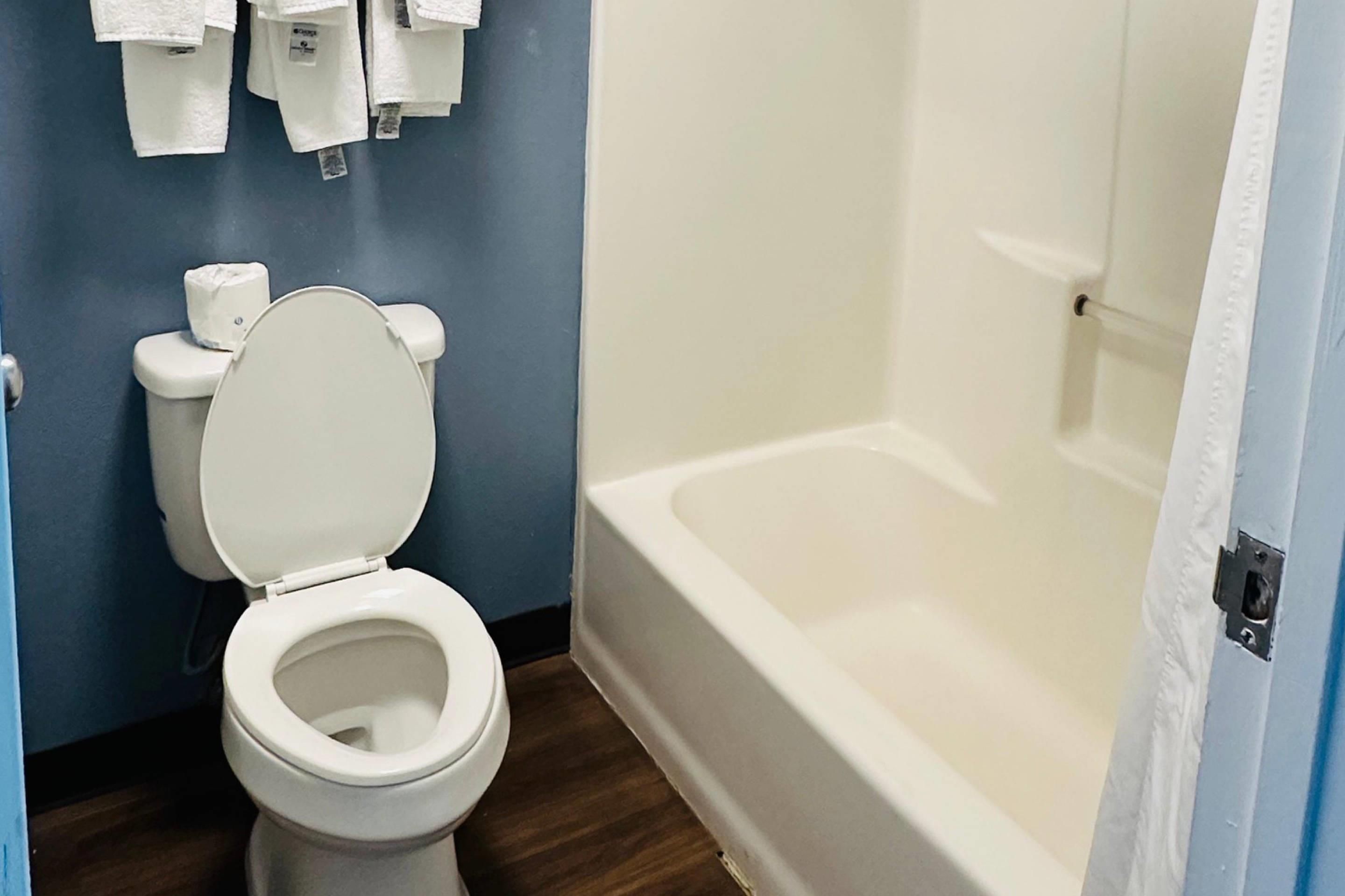 Un baño con inodoro, bañera y dispensador de papel higiénico en la pared.