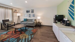 A modern hotel room with a sofa, armchair, coffee station, and a desk. - Woodspring Suites Dayton North (Dayton)