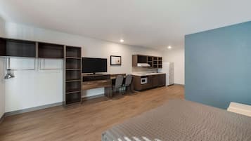 A modern bedroom with a bed, a desk, a chair, and a kitchenette.