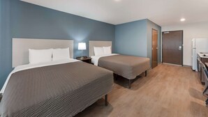 A hotel room with two beds, a desk, a chair, a lamp, and a door. - Woodspring Suites Dayton North (Dayton)