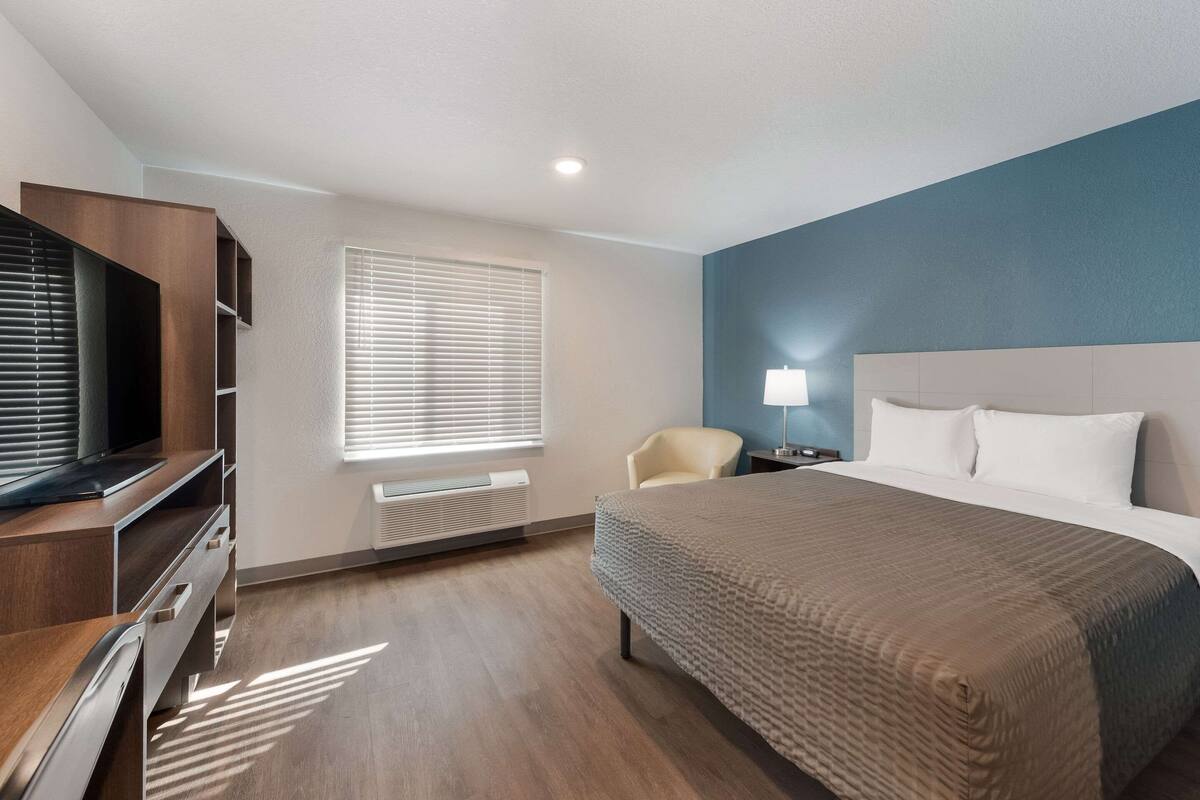 Une chambre d’hôtel équipée d’un lit, d’une télévision, d’une chaise, d’un bureau et d’une fenêtre avec des stores.