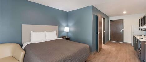 A bedroom with a bed, bedside table, lamp, and a chair.