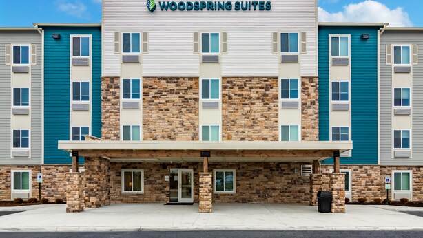A multi-story hotel with a stone facade, a covered entrance, and a sign reading "Woodspring Suites". - Woodspring Suites Dayton North (Dayton)
