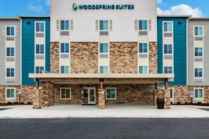 Un hôtel à plusieurs étages, doté d’une façade en pierre, d’une entrée couverte et d’une enseigne indiquant « Woodspring Suites ».