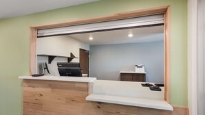 A reception desk with a wooden finish, a sliding door, and a view into a room with a desk and a chair. - Woodspring Suites Dayton North (Dayton)