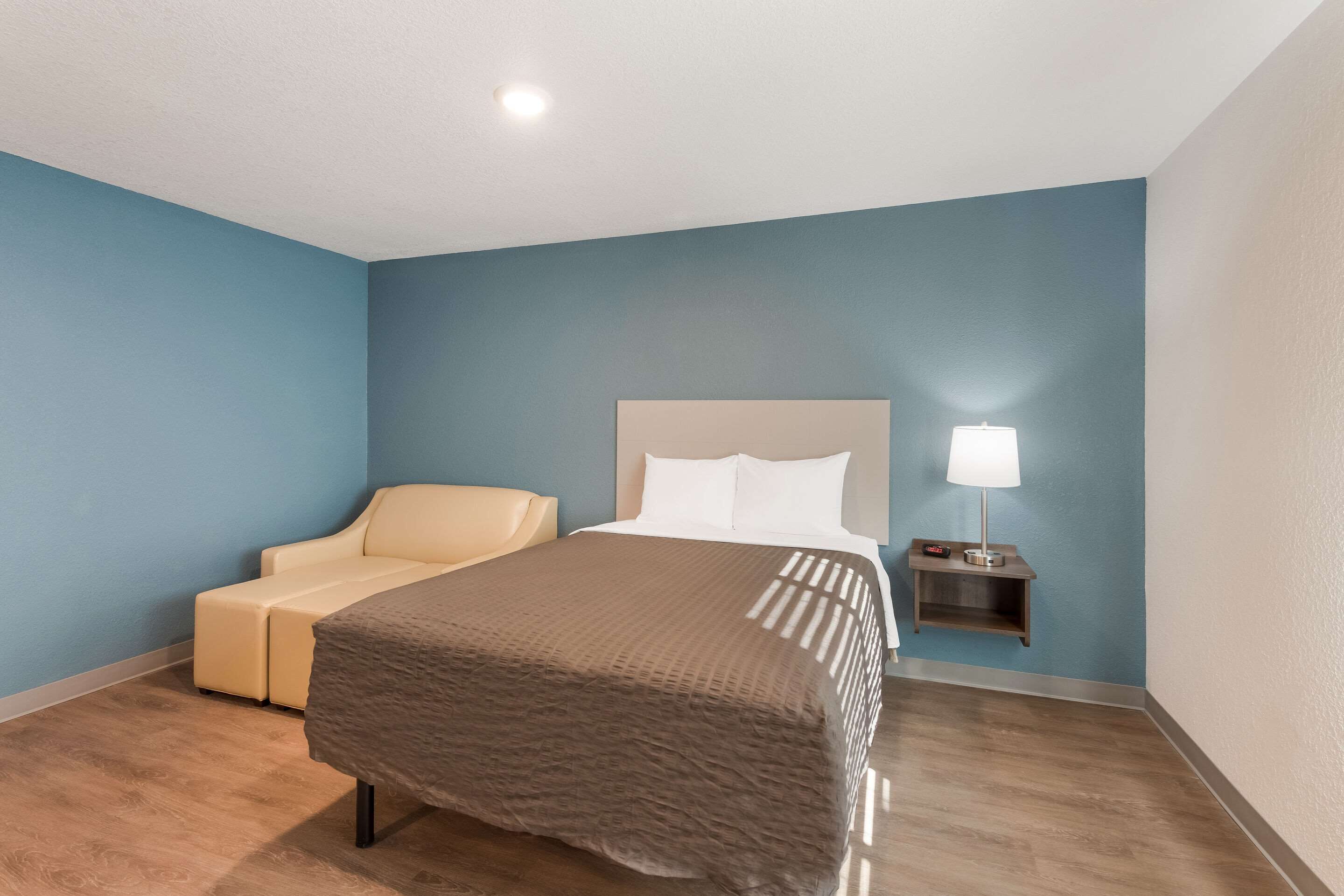 Une chambre d’hôtel avec un lit, une chaise, une table de chevet avec une lampe et un mur bleu.