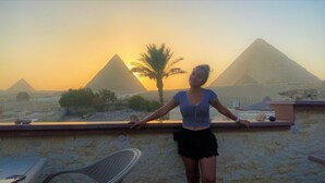 A person standing on a balcony with a view of the pyramids at sunset. - Double Room with Balcony Pyramids View (الهرم)