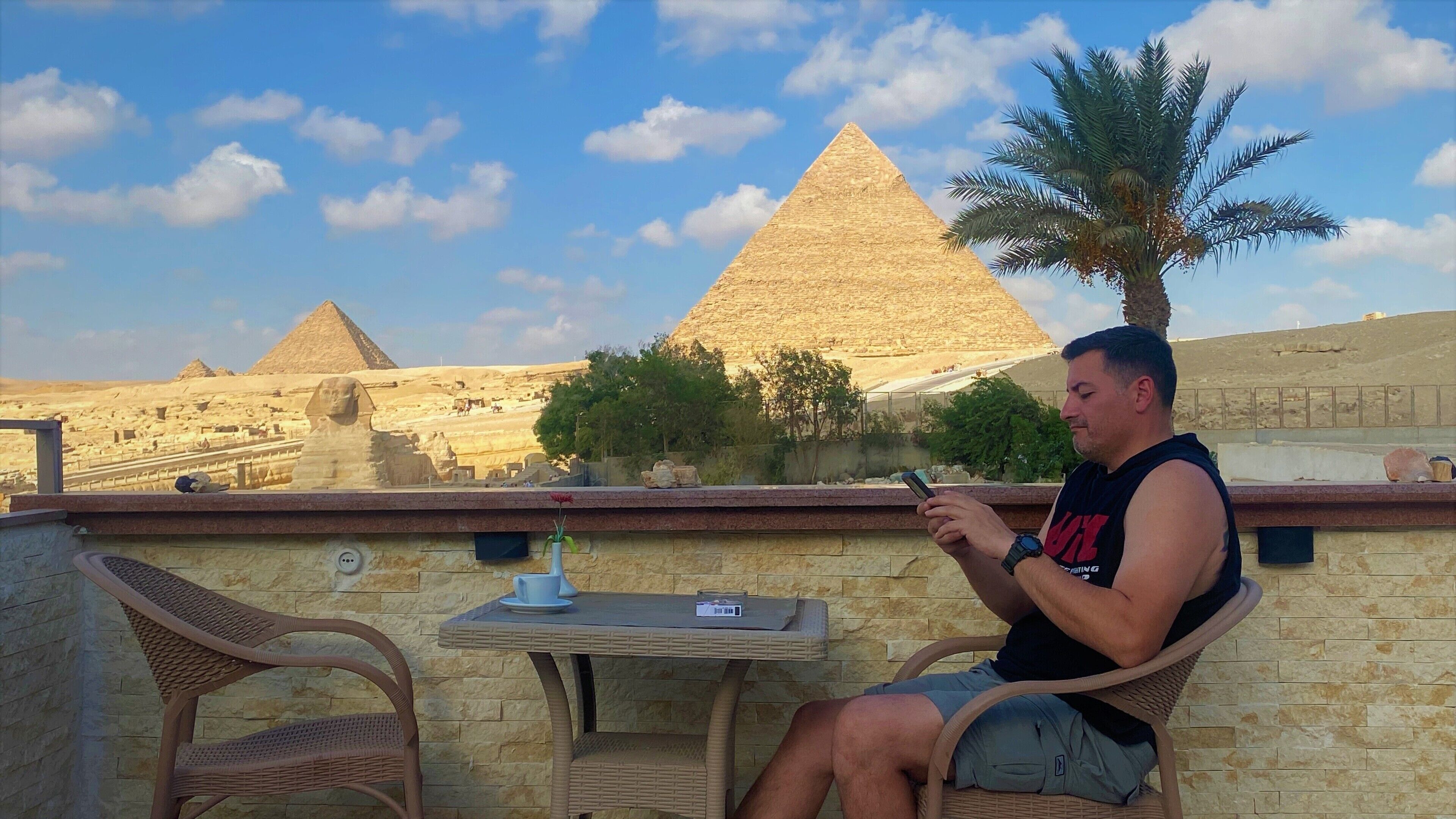 A man seated at a table with a view of the pyramids.