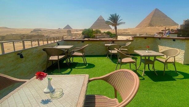 A rooftop terrace with wicker furniture and a view of the pyramids. - Double Room with Balcony Pyramids View (الهرم)