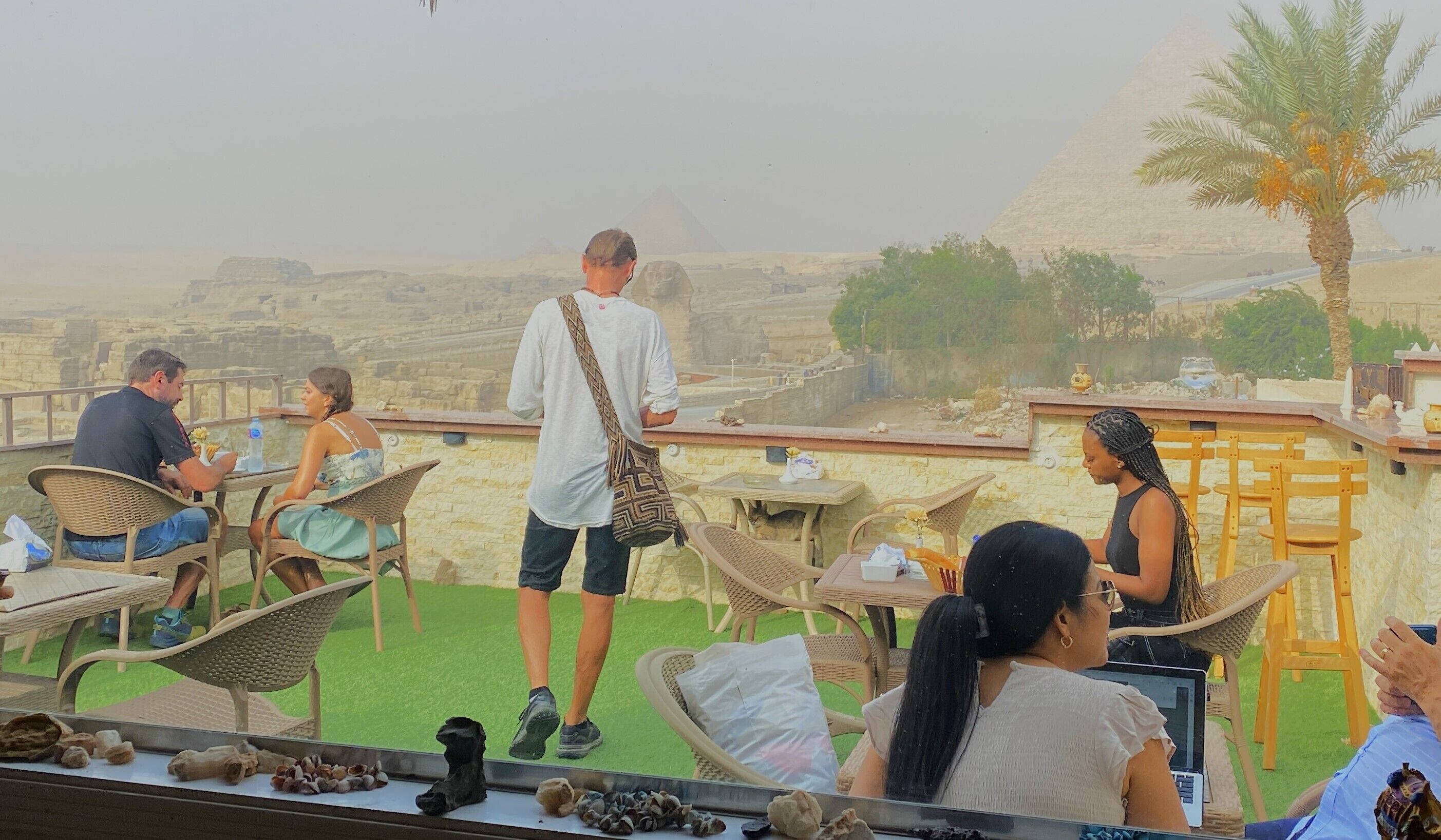 A terrace with wicker chairs and tables, overlooking a mountainous landscape.