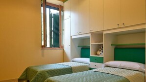 Una habitación con dos camas individuales, una ventana con persianas y un cabecero verde.