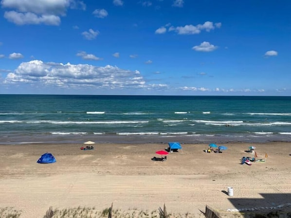 A beach with tents and umbrellas, a clear sky, and the ocean. - Gorgeous Oceanfront Condo, heated pool, garage (South Padre Island)
