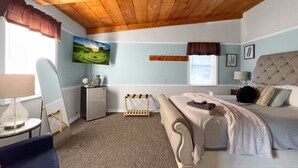 Un dormitorio con cama, escritorio, silla, televisor y un cuadro en la pared.