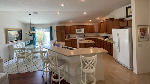 A modern kitchen with wooden cabinets, a white refrigerator, and a central island with bar stools. - ESCAPE! to The Villages...Villa with Golf Car! (The Villages)