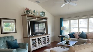 A living room with a television, a sofa, a chair, a coffee table, and a cabinet. - ESCAPE! to The Villages...Villa with Golf Car! (The Villages)