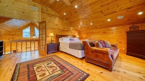 A cozy log cabin bedroom with a large bed, a leather sofa, and a wooden dresser. - River Mornings, Hot tub Evenings, Repeat (Suches)