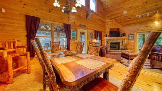 A wooden cabin interior with a dining area, leather seating, a fireplace, and a mounted deer head. - River Mornings, Hot tub Evenings, Repeat (Suches)