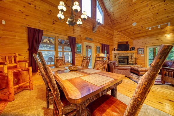 Interior d'una cabana de fusta amb zona de menjador, seients de cuir, una llar de foc i un cap de cérvol penjat.